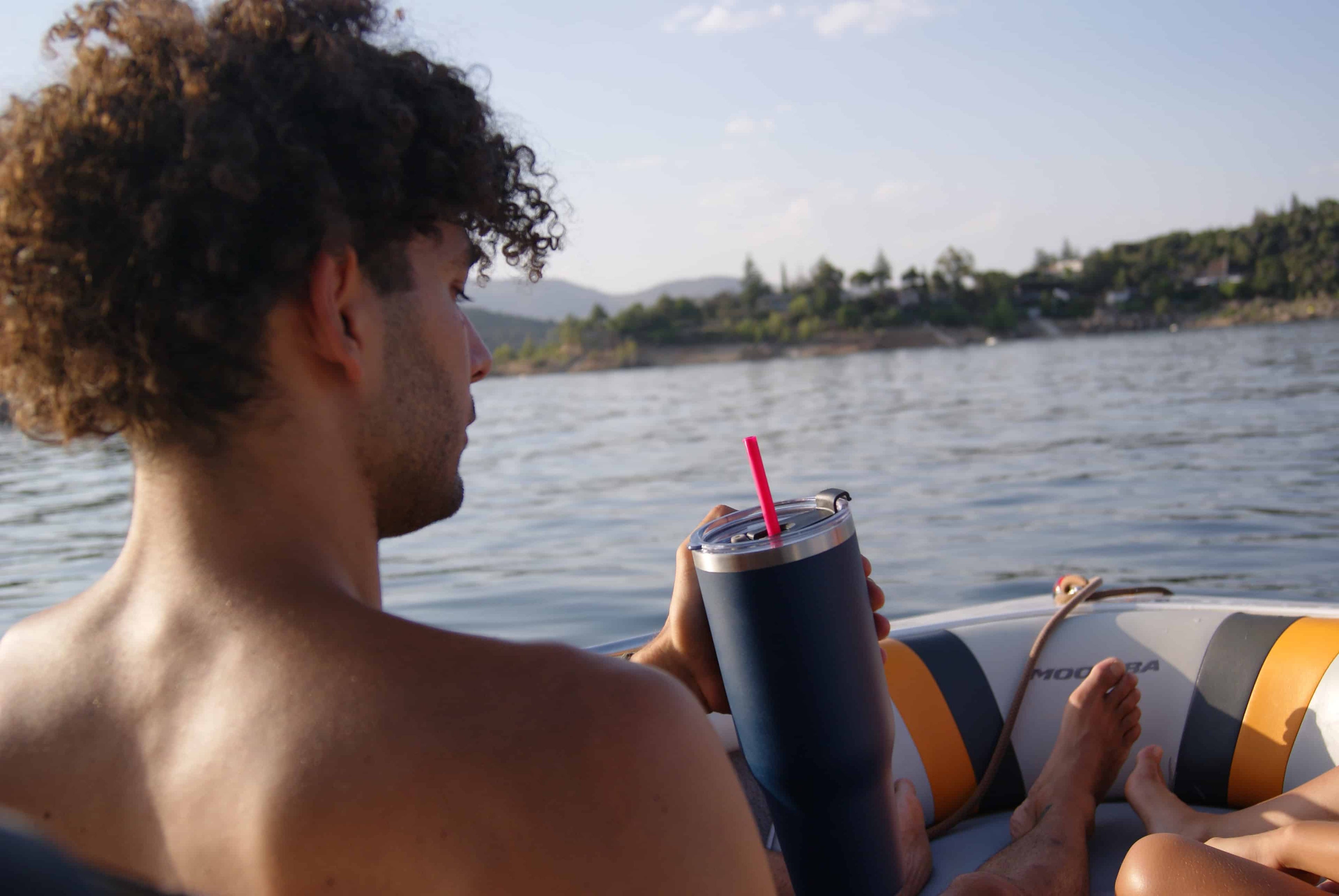 Hombre sentado en la parte delantera de un barco, mirando al horizonte con su taza térmica de acero inoxidable Dipso en la mano.